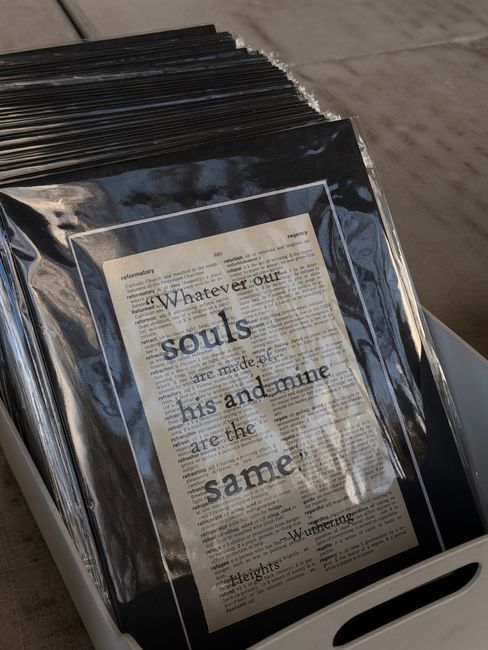 Close-up image of a black plastic rubbish bag, tightly knotted at the top, resting against a plain, light-colored wall. The bag appears to be made of shiny, durable plastic with visible creases and sl